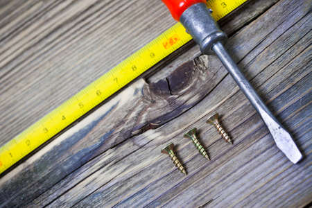 antique screwdriver, screws and measuring lenght on old textured boards ancient bench