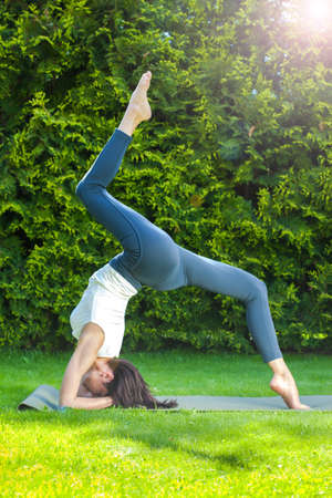 beautiful adult woman doing yoga on a green grass at summer morning in park