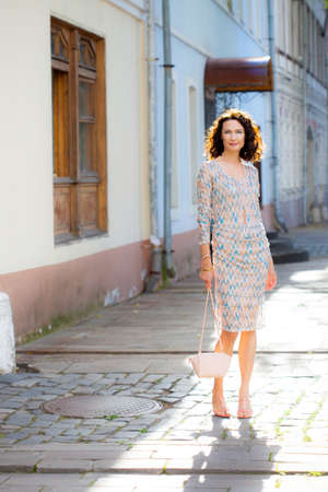 smiling beautiful middle-aged woman with a small handbag on the ancient streetの写真素材