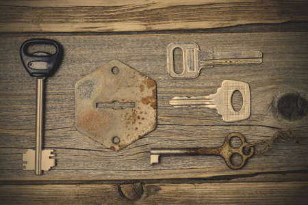 A set of lost keys and an old keyhole on a wooden textured surface. instagram image filter retro styleの写真素材
