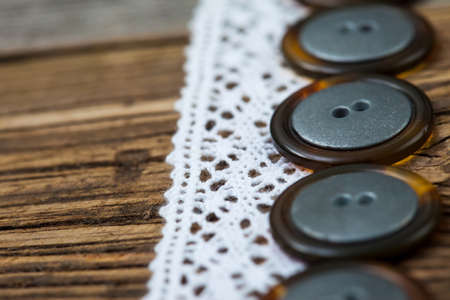 Vintage lace ribbons and buttons set on an old wooden table, close up. Shallow depth of field