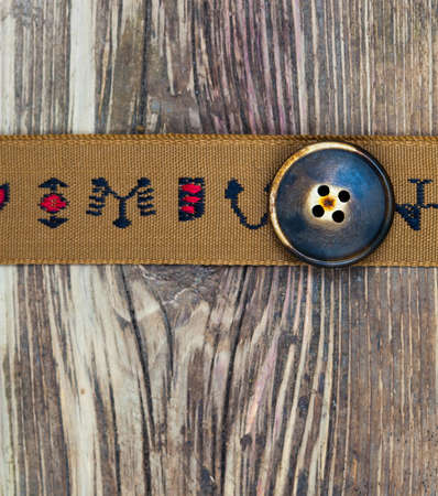 vintage band with embroidered ornaments and old button on a textured surface aged boards