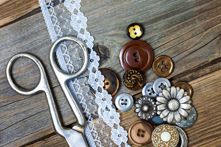 vintage buttons, lace, and a dressmaker scissors on a textured surface of old boardsの写真素材