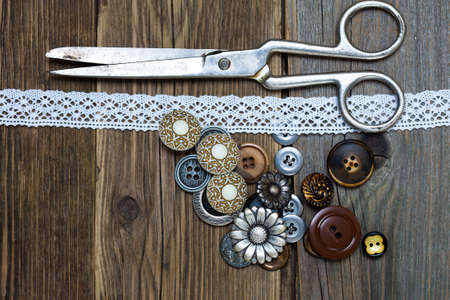antique buttons, lace and a tailor scissors on a textured surface of old boards