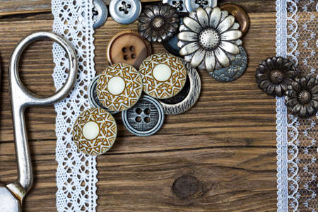 vintage buttons, lace, and a tailor scissors on a textured surface of old boardsの写真素材