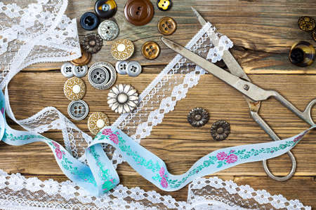 vintage buttons, lace, and a dressmaker scissors on a textured surface of old boardsの写真素材