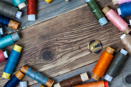 one vintage button and coils of different threads on the surface of an old tailors table
