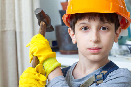 Boy in the image of a builder in a protective helmet with a hammerの写真素材