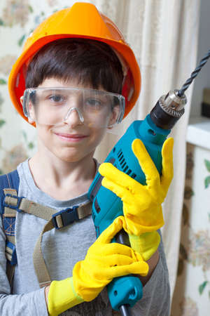 Smiling boy builder in goggles and with a drill in his handsの写真素材