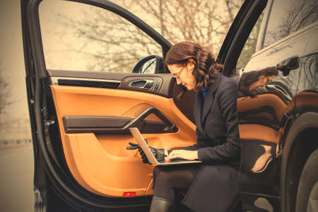 dark haired woman with a laptop sit on the step of the car with the door open. image filter retro styleの写真素材