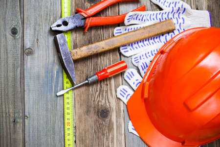 Vintage hammer, pliers, screwdriver, tape measure, a bright helmet and gloves on an old wooden...