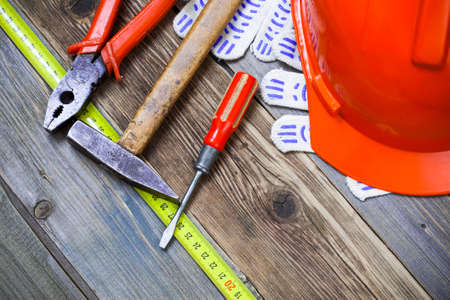 Vintage hammer, pliers, screwdriver, tape measure, a bright helmet and gloves on an old wooden...