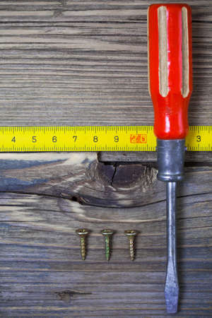screwdriver, screws and measuring tape on old textured boards ancient bench