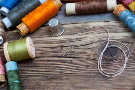 vintage spool of thread, a thimble and a sewing needle on old boards