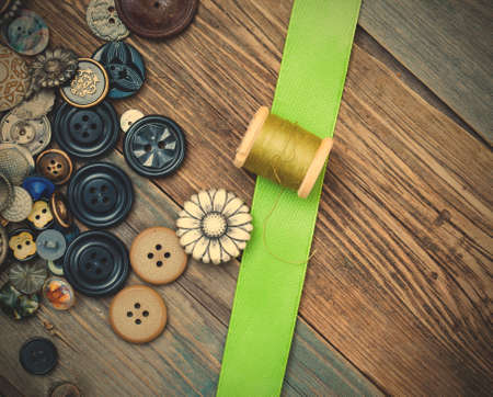 vintage buttons, spool with thread and green tape on aged textured boards.の写真素材