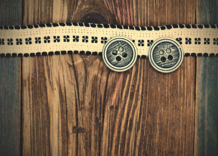 Vintage ribbon with embroidered pattern and ancient classical buttons on the old textured boards.の写真素材
