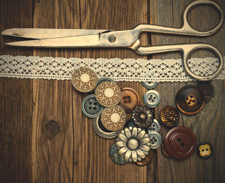 antique buttons, lace and a tailor scissors on a textured surface of old boards.