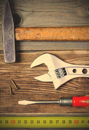 old screwdriver, screws, monkey wrench, vintage hammer and tape-measure on the boards of the old workbench.  image filter retro styleの写真素材