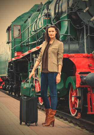 beautiful adult woman traveler with a suitcase on the platform near the vintage steam locomotive.  image filter retro styleの写真素材