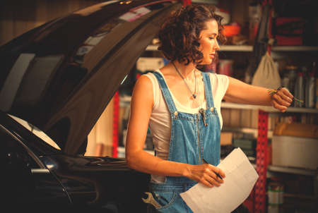 beautiful woman car mechanic in blue overalls looks at wristwatch.の写真素材
