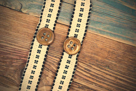 two vintage band with embroidered ornaments andÂ old button on a textured surface aged boards.