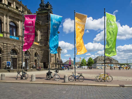 Dresden, Germany-June 7, 2017: Side view on the Semper Opera with the vibrant blue sky and white clouds. Colourful banners and bikes in the foreground.のeditorial素材