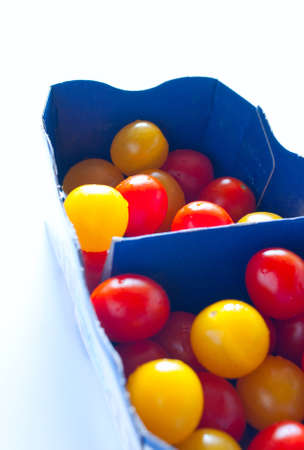 Blue cardboard box full of red and yellow cherry tomatoes on whiteの写真素材