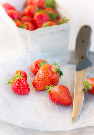 Fresh strawberries on the wax paper  One of them cut in two halves with a knifeの写真素材