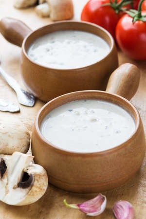 Creamy mushroom soup in two clay pots on a wooden tableの写真素材