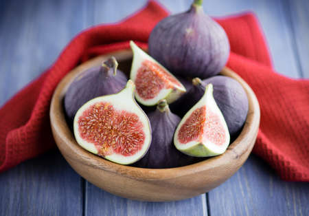 Group of figs in a bowl on rustic blue wooden table with a red towelの写真素材