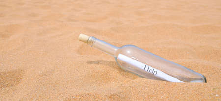 Bottle with a message inside help on beach sandの写真素材