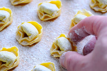 Preparing homemade tortellini on wooden table in the kitchen.