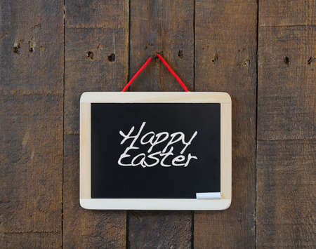 Blackboard hanging on a old wooden wall with word Happy Easter.の写真素材