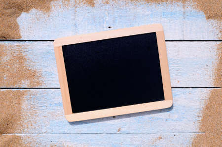 Blackboard and blue wooden table on beach sand.の写真素材