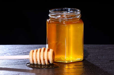 Close-up of jar of honey and wooden stick on table against of black background.