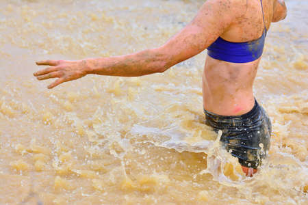 Woman walking in dirty water making splashes. Unrecognizable