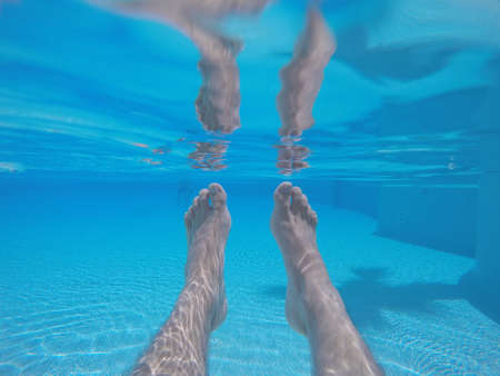 Underwater shot of male feet in blue clear swimming pool water in sunlight