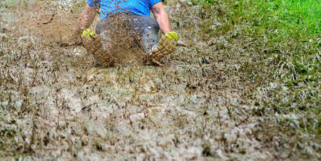 Unrecognizable man sliding the muddy slope making dirty splashes around