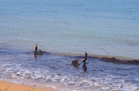 LUANCO, SPAIN - APRIL 22, 2017: People pick up seaweed on a beach in Luanco, Spain on April 22, 2017.のeditorial素材
