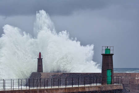 Stormy wave over old lighthouse and pier of Viavelez in Asturias, Spain.の写真素材