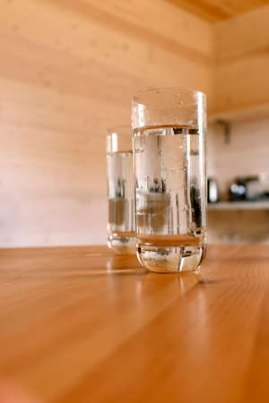 Two glass glasses with water on a wooden table in a wooden house on a summer day.の写真素材