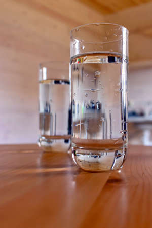 Two glass glasses with water close-up on a wooden table in a wooden house on a summer day.の写真素材