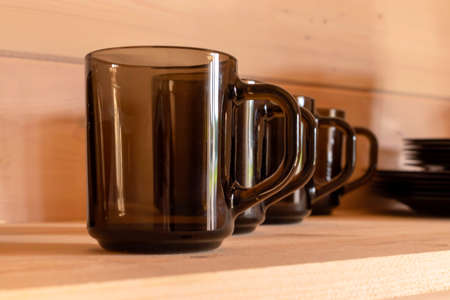 Mugs made of brown translucent glass stand in a row on a wooden shelf.の写真素材