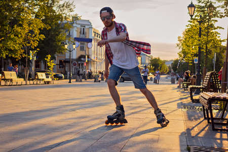 A young man with a beard on the street on the cobblestones rollerblading at sunset.の写真素材