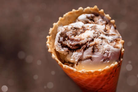 Waffle cone with coconut-chocolate ice cream on a brown background with bokeh on a sunny day.の写真素材