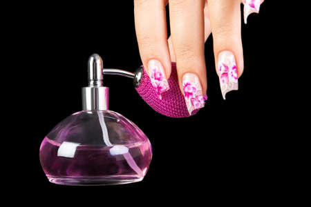 The female hand with beautiful nails holds a bottle of perfume, on a black background