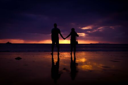 Silhouette of couple hold each other hand and Happy Young Couple love on the beach at sunset timeの写真素材