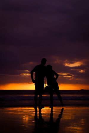 Silhouette of couple hold each other hand and Happy Young Couple love on the beach at sunset timeの写真素材