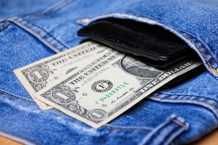 Black leather wallet with money in back blue jeans pocket denim background texture.