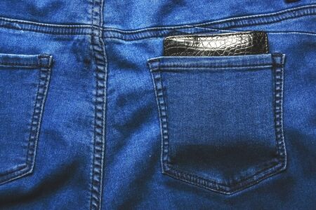 Black leather wallet in back blue jeans pocket denim background texture.